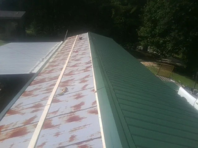 Old rusted panels beside newly installed green metal roofing in Guilford